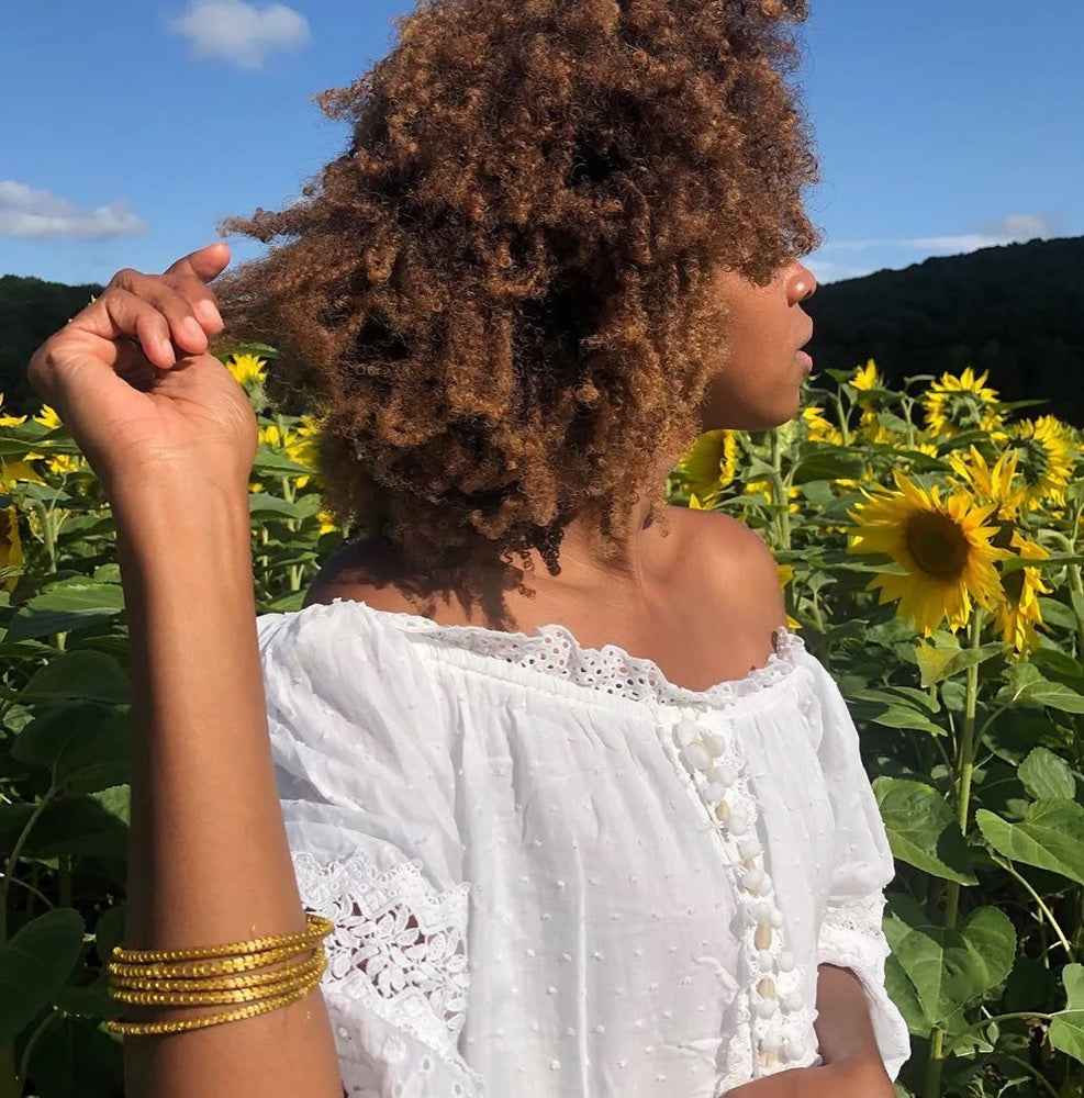 Joncs dorés ORA portés au poignet dans un champ de tournesols