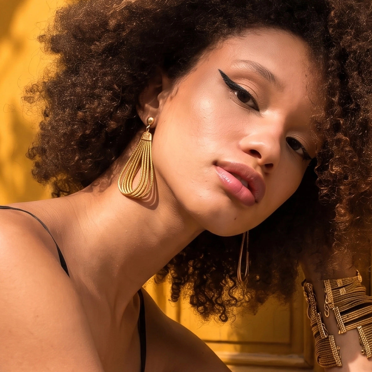 Boucle d'oreille Gota ORA portée, gros plan à l'oreille devant une porte parisienne moutarde