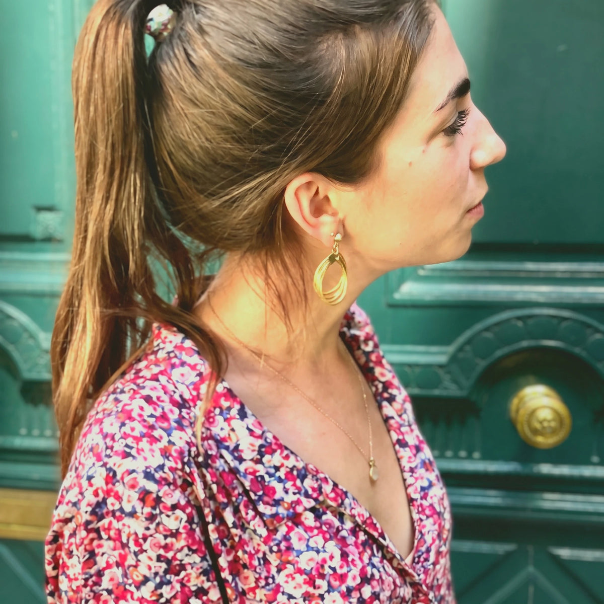 Boucles d'oreilles Lola ORA portées avec un chemisier fleuri, devant une porte cochère parisienne