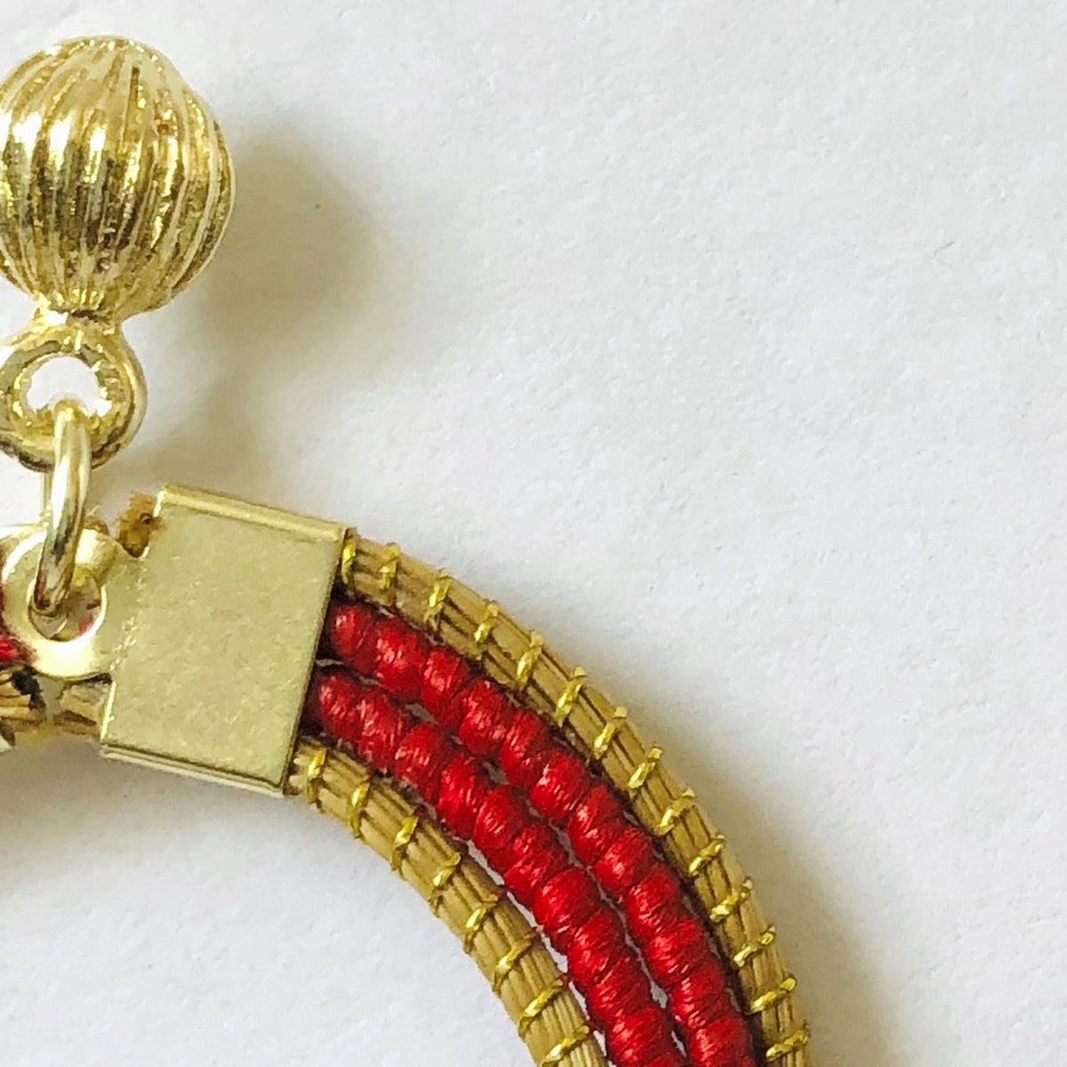Détail de la perle dorée côtelée et du tressage rouge des Lola Arco-Íris ORA